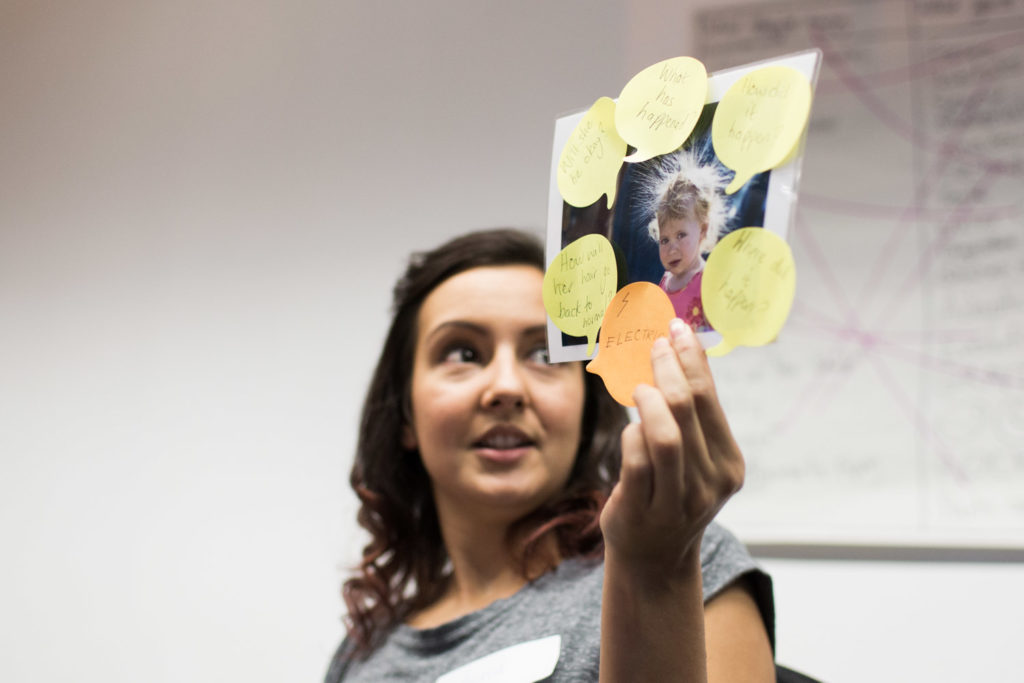A female teachers' course participant holds up a picture with neon post-it notes attached to the edges