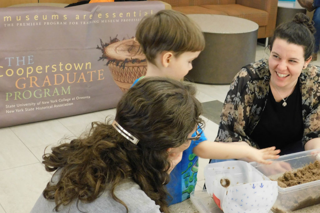 A child and mother interacting with a Cooperstown Graduate Program student at their stand at the Explore Science fair.