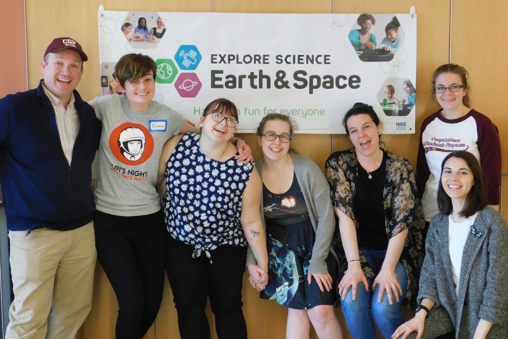 A group of Cooperstown Graduate Programme students smiling in front of their Explore Science Earth & Space fair banner.