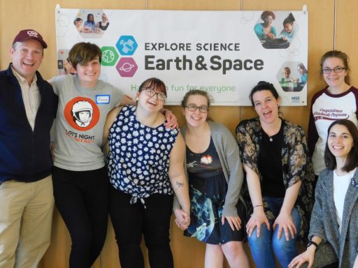 A group of Cooperstown Graduate Programme students smiling in front of their Explore Science Earth & Space fair banner.