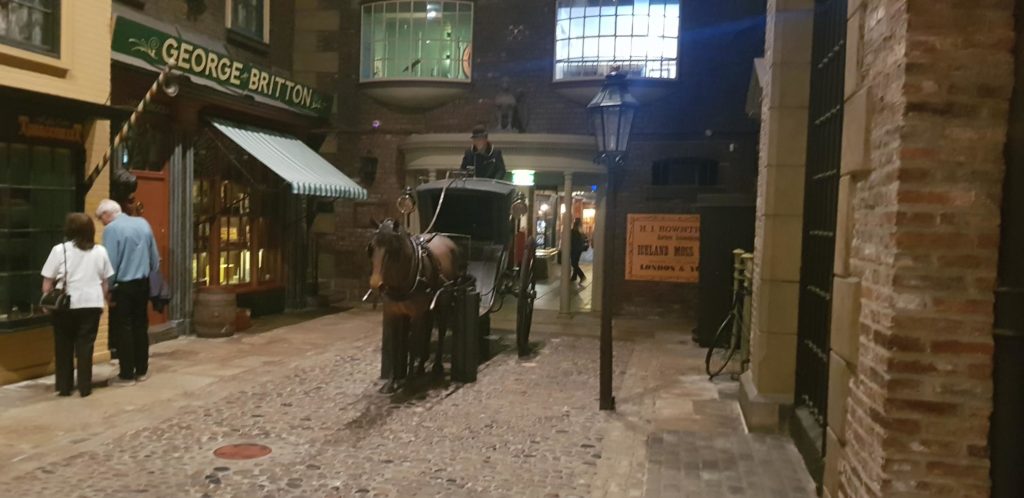 The Victorian street inside the castle museum. There are two people looking a shop window on the left and a horse and coach in the centre of cobbled streets. 