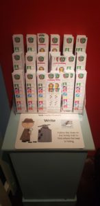 A display stand which holds a museum trail. The trails are tall and thin like a bookmark with images of toys you need to find.