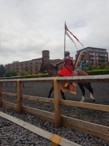 A man in a red outfit carrying a flag riding a horse. 